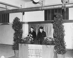 Rabbi Samuel Snieg (right), head of the Central Committee of Liberated Jews, stands at the podium during  opening ceremonies for the first Jewish bakery in Berlin since the end of the Nazi period.