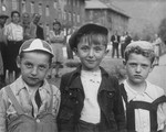 Portrait of three young Jewish boys wearing caps standing outside in the Bad Reichenhall displaced persons camp.