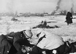 Three German soldiers inspect a document in a snowy field while another views a burning village in the distance [probably in the Soviet Union].
