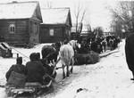 German soldiers ride in a caravan of horse-drawn sleighs past wooden homes in a village [probably in the Soviet Union].