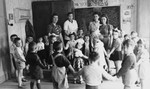 Preschool children dance in a circle in a classroom in the Wels DP camp.