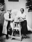 Sculptors Naum Aronson and Miriam Berlin pose on either side of a stool in Aronson's studio in Paris.