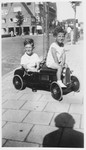 Two young Jewish boys ride a toy car on a sidewalk in Amsterdam.