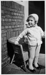 A young Jewish girl who is living in hiding in the home of her aunt and uncle, poses next to a wicker chair.