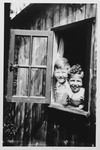 Two young Jewish brothers peer out from a window of a wooden cabin.