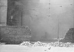 Smoke fills the street beyond the breached ghetto wall as apartment buildings razed by the SS burn during the suppression of the Warsaw ghetto uprising.
