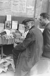 Book vendors sit in front of a table piled with books on a street in the Warsaw ghetto.
