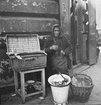 A woman vendor on the street in the Warsaw ghetto offers pickles and food for sale.