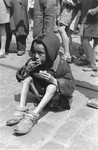 A destitute child eats a crust of bread while sitting on a street in the Warsaw ghetto.