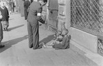 A man stops to help two destitute children on the street in the Warsaw ghetto.
