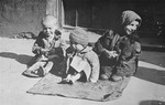 Three destitute young children sit on the pavement in the Warsaw ghetto.