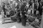 Jews gather around a couple selling kindling on the street in the Warsaw ghetto.