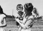 A woman poses holding a child in a field at a Jewish displaced persons camp in Austria (probably Bindermichl).