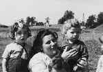 A woman poses with pre-school age children outside in a field at a Jewish displaced persons camp in Austria (probably Bindermichl).