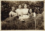 Four young people and a young baby sit on top of a hay wagon.
