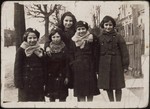 Five school girls wearing winter coats stand together on a street in Eisiskes.