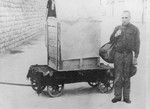 An escaped Mauthausen prisoner who has been apprehended by the SS is forced to pose next to the box in which he attempted his escape.