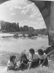 A group of girl scouts play recorders on a riverbank.