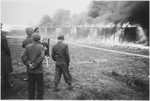 British soldiers watch as fire consumes a barracks in the Bergen-Belsen concentration camp.
