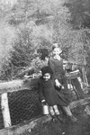 A Jewish brother and sister who are living in hiding in Boissy-Saint-Leger, France, pose outside near a wire mesh fence.