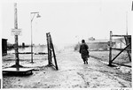 An American soldier walks through the gates of the Kaufering I (Landsberg) concentration camp on the day of liberation.