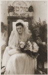 A young Jewish bride poses with a bouquet of flowers beneath a Hebrew sign reading "Mazel Tov" (Congratulations) [probably at the Fuerth displaced persons camp].