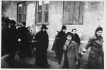 Jews wearing armbands are gathered outside a partially boarded-up building in the Warsaw ghetto.