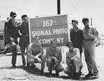 Group portrait of members of the U.S. army 167th Signal Photo Company in front of a sign identifying their company.