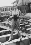 Portrait of U.S. combat photographer Arnold E. Samuelson holding a Speed Graphic camera while standing in a boat.