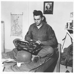 U.S. combat photographer J Malan Heslop types photo captions on a typewriter in his room.