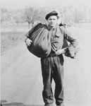 Portrait of a young, male displaced person walking with a large sack along a road in Austria at the close of World War II.