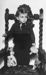 Portrait of a young Jewish boy standing on an ornate wooden armchair.