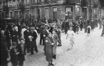 Large numbers of Jews walk along a street in the Warsaw ghetto.