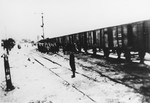 A German stands guards on a snow-covered railroad track as a group of Jews are led to a deportation train.