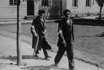 Two Jewish men wearing armbands walk along a path in Konskowola.