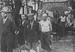 A group of Jewish men stand among furniture and hanging laundry in the Kutno ghetto.