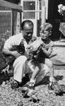 A Jewish child and his Indonesian-Dutch rescuer sit outside holding chickens during a postwar visit.