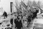 Jewish survivors carrying flags march along a street in Warsaw [probably during a demonstration marking the fourth anniversary of the Warsaw ghetto uprising].