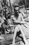 An emaciated survivor sits by a portable shower set up by the 30th U.S.