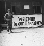 Eugene Cohen stands in front of a banner offering "Welcome to our liberators" in the Mauthausen concentration camp.