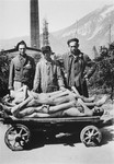 Survivors in the Ebensee concentration camp stand next to a cart stacked with the bodies of former prisoners.