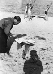 A prisoner in the Saint Cyprien internment camp paints a picture outside on a sandy beach.