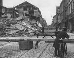 A boy with a bicycle stands at a barrier closing off a heavily damaged street in a German city.