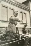 Hitler points at something while standing in his car [during an official procession].