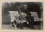 A grandfather sits next to his two grandchildren on a park bench.