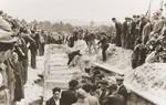 Mourners and local residents watch as men shovel dirt into the mass grave of the victims of the Kielce pogrom.