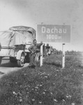 Melvin Hamamoto, a Japanese-American liberator, poses next to a road sign outside of Dachau as trucks with the 522nd Field Artillery Battalion press on towards the town.