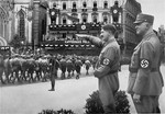 Adolf Hitler salutes passing SA troops while their commander, SA Reichstatthalter of Saxony, Mutschmann, looks on.