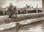 Two soldiers from the 42nd Rainbow Division and a liberated prisoner fish the body of an SS guard out of the moat surrounding the Dachau concentration camp.