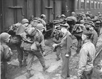 General Dwight D. Eisenhower talks to US troops who are marching with their gear alongside a train.